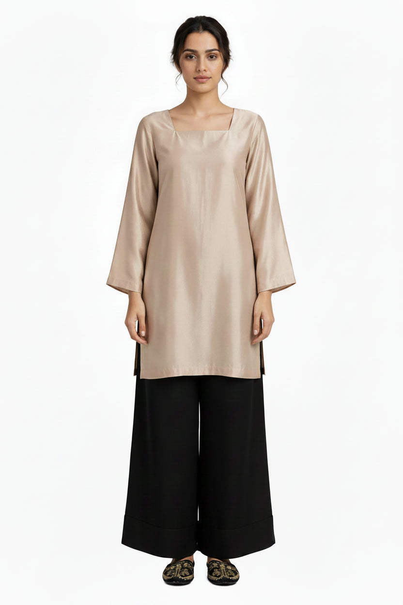 A woman stands against a plain white background wearing a light beige tunic with a square neckline and wide three-quarter sleeves, paired with loose black wide-leg pants.