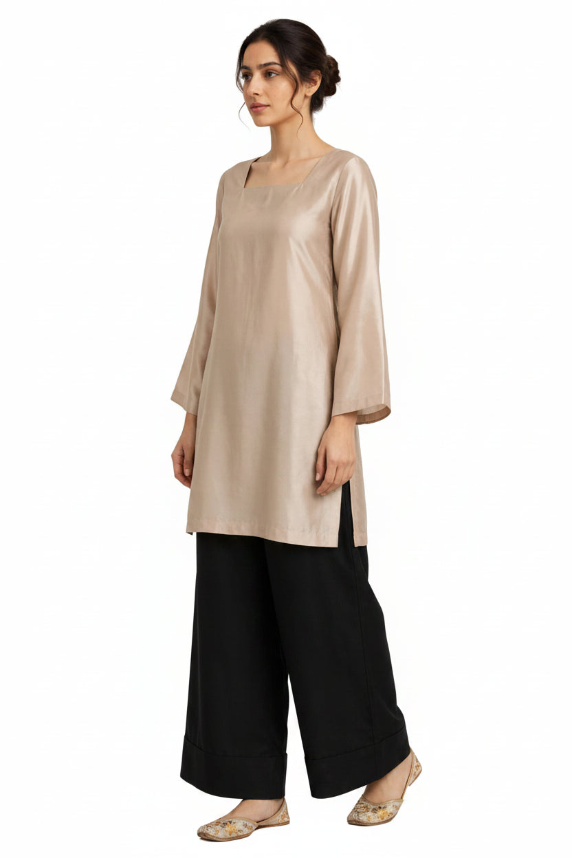 A woman modeling a light beige tunic top with three-quarter sleeves and black wide-leg pants against a plain white background.