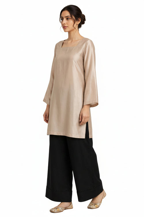 A woman modeling a light beige tunic top with three-quarter sleeves and black wide-leg pants against a plain white background.