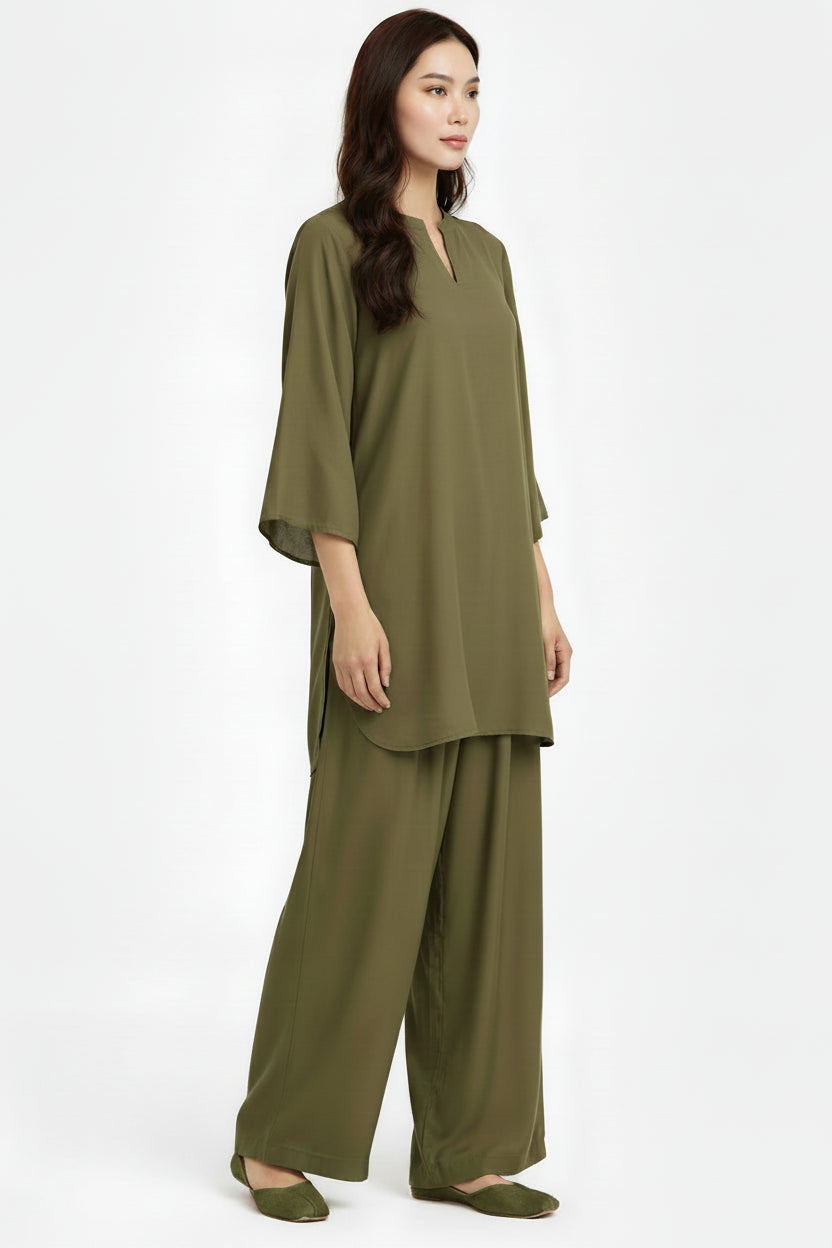 A woman modeling a matching olive green two-piece lounge set consisting of a short-sleeve tunic top with a split neckline and wide-leg pants, photographed against a plain white studio background.