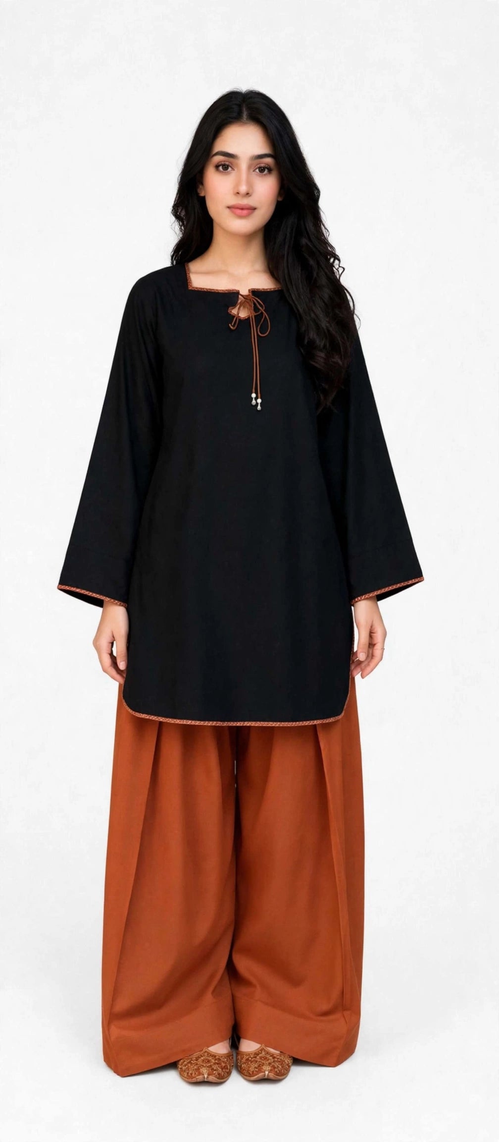 A woman modeling a black tunic with wide three-quarter sleeves and a drawstring neckline, paired with rust-orange wide-leg pants, against a plain white studio background.