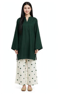 A woman modeling a dark green long-sleeve tunic with a split neckline, paired with off-white wide-leg pants featuring a green heart pattern, against a plain white background.