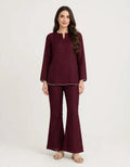 A woman modeling a matching deep burgundy two-piece set consisting of a long-sleeve tunic top with a split neckline and matching flared pants, styled with neutral sandals against a plain light background.